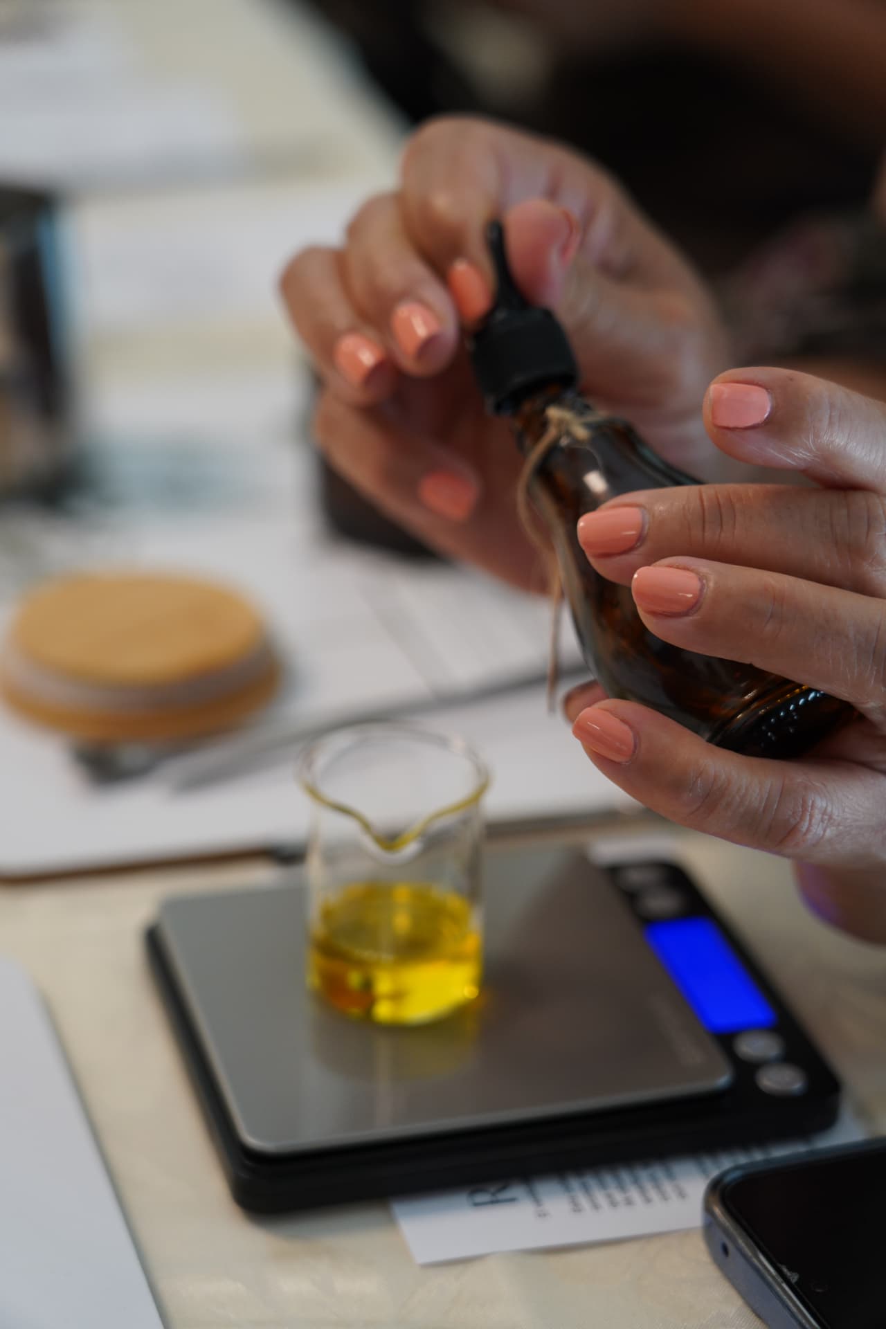 Amber essential oil bottle held over a small glass beaker on a digital scale