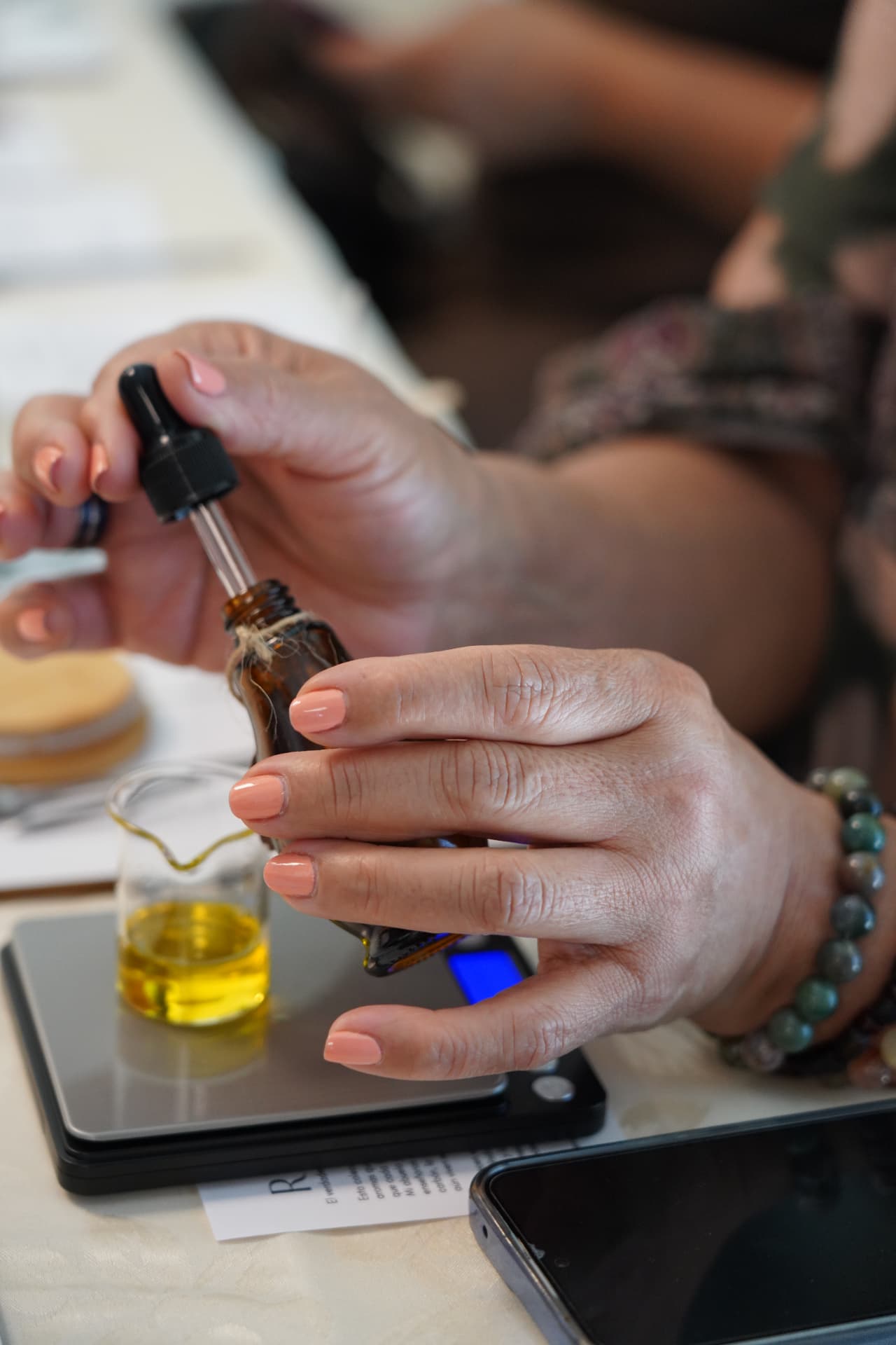 A glass pipette returning to an amber essential oil bottle at a workshop table